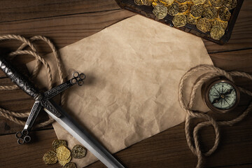 Blank old paper page with copy space. Chest with golden coins, rope and a compass on a wooden...
