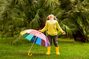 a beautiful girl in a yellow sweater and yellow boots, walking in the park with a colored umbrella