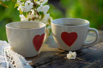 Coffee with milk, cocoa, tea in cups with heart decor, lace napkin on a wooden table. Cherry blossoming branches, spring mood. Outdoor brunch refreshments.