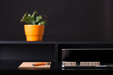 Close up view of a black work desk interior with a laptop computer, a cup of coffee,  paper,pen and a cactus with flowers.