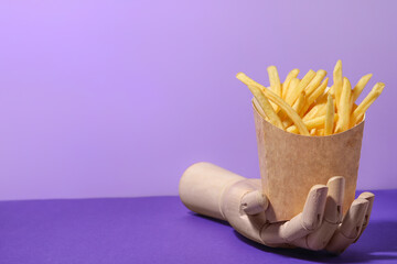 Wooden hand with tasty french fries on color background