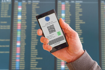 Mobile phone with digital green certificate of vaccination covid-19. Cell Phone screen with information on vaccination and antibodies to covid against the background of the scoreboard at the airport