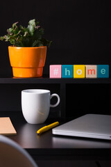 Close up view of a black work desk interior with a laptop computer, a cup of coffee,  paper,pen and a cactus with flowers.