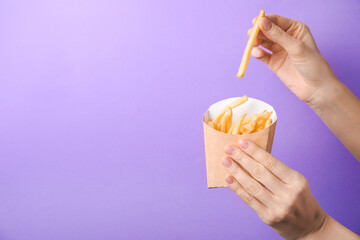 Woman eating tasty french fries on color background