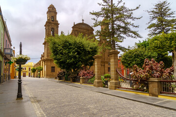 Naklejka premium Old church next to a park with green plants and cobbled streets. Galdar Gran Canaria.