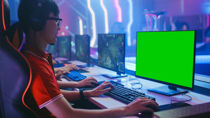 Professional Gamer Plays in a Video Game with Mock-up Green Screen Display on a Championship. Team of Pro Gamers in Stylish Neon Cyber Games Arena. Online Broadcasting of Tournament. Side View Shot © Gorodenkoff
