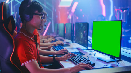 Professional Gamer Plays in a Video Game with Mock-up Green Screen Display on a Championship. Team of Pro Gamers in Stylish Neon Cyber Games Arena. Online Broadcasting of Tournament. Side View © Gorodenkoff