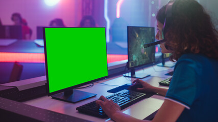 Pro Girl Plays Computer Video Game with Green Screen Display on Championship, Talking into Headset. Diverse Esport Team of Pro Gamers Play in Mock-up Video Game. Cyber Games Arena. Over the Shoulder © Gorodenkoff