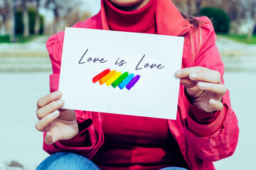 woman holding sign with the slogan love is love and the flag with the LGTBIQ colors red, orange, yellow, green, blue and purple