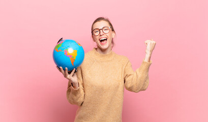 young blond woman shouting aggressively with an angry expression or with fists clenched celebrating...