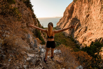 rear view of woman with arms to sides standing on stone and enjoying on view of landscape.