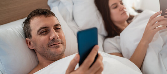 Couple laying in the bed and using smartphone