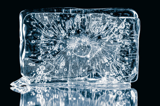 Piece of pure ice in rectangular shape form with air bubbles on a black background on a reflective surface.