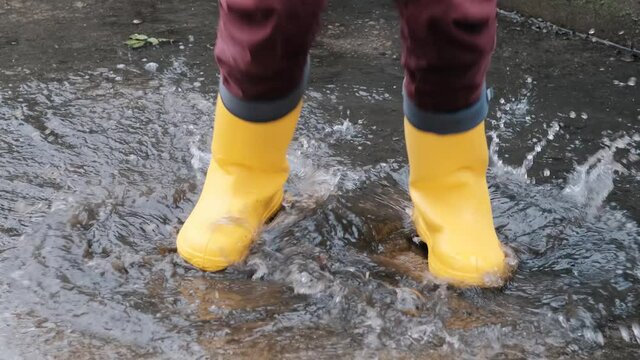 Jump through puddles in yellow rubber boots. Walk in rain and enjoy the bad weather falling into childhood and running through wet puddles. Video of legs without face.