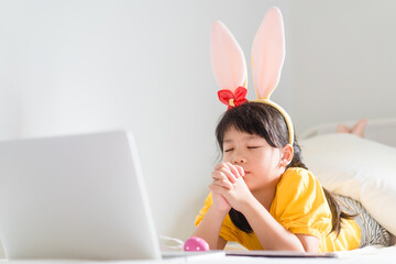 Happy easter day.Asian child girl in rabbit ears pray.Faith prayer Online worship in easter day home.Kid with faith trust.Healthcare, easter worship home church.Lockdown, covid19 coronavirus.online.