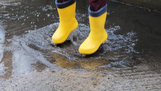 Jump through puddles in yellow rubber boots. Walk in rain and enjoy the bad weather falling into childhood and running through wet puddles. Video of legs without face.