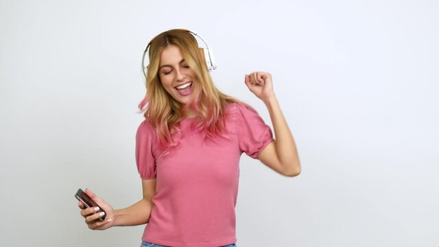 Young blonde woman  listening music with a mobile and dancing over isolated background