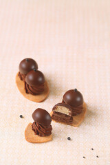 Shortcrust Oval Cookies with Chocolate Cream and Praline Bonbons on Top, on a light beige background.