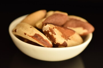 Several ripe organic Brazil nuts in a white saucer, close-up. The background is black.