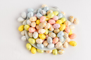 Mixed chocolate coated Easter eggs candies on a small plate isolated on a white table, tasty sugary dessert for children.
