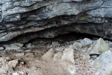 a stone entrance to the cave. karst failure in the ground. dark black hole deep in the cave. mountainous terrain. winter in the mountains.