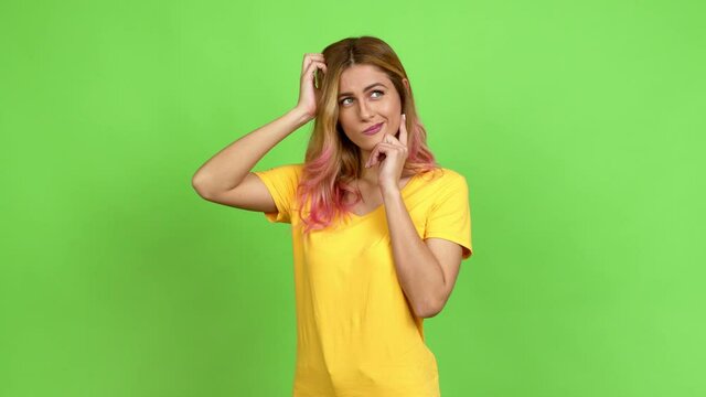 Young blonde woman having doubts while scratching head over isolated background on green screen chroma key