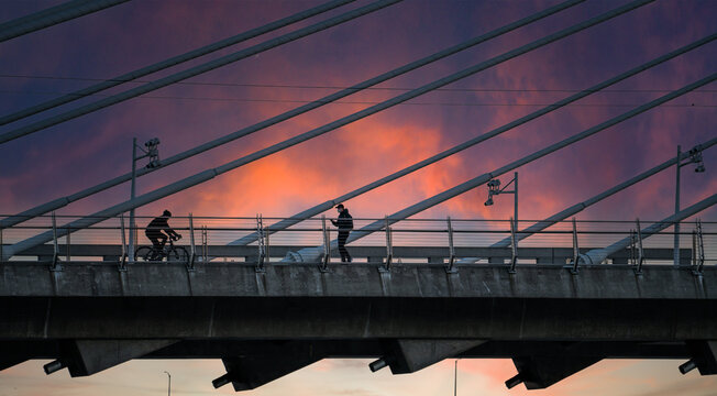 Portland, Oregon - 2-11-2021: A man on a bicycle and man walking on the pedestrian path at sunset on the Tilikum cable stayed bridge over the Willamette River  in Portland Oregon