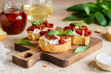 Bruschetta with sun dried tomatoes, cream cheese and basil on a wooden board. Selective focus