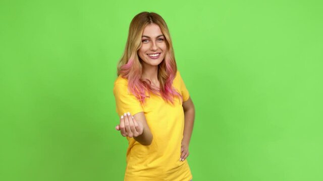 Young blonde woman presenting and inviting to come with hand over isolated background on green screen chroma key