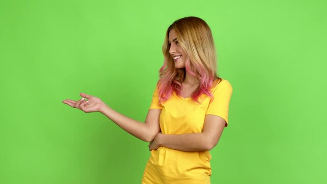 Young blonde woman extending hands to the side and inviting to come over isolated background on green screen chroma key