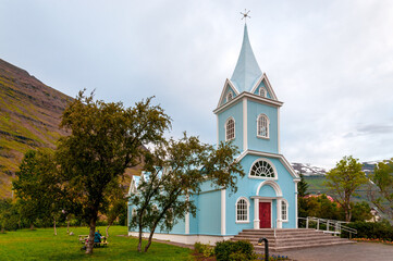 Fototapeta na wymiar Light blue Lutheran church of Seyðisfjörður (Seyðisfjarðarkirkja) surrounded by a garden with green grass and fruit trees. Iceland