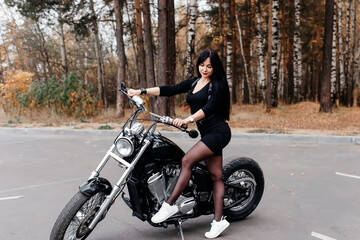 Naklejka na ściany i meble beautiful brunette in a dress on a motorcycle in the park