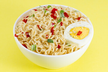 Instant noodles with vegetables and herbs in bowl on yellow background