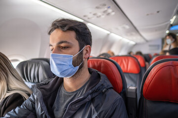 young man with mask sitting on aircraft seat among many passengers in plane in quarantine days