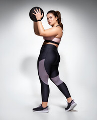 Fototapeta na wymiar Strong woman workout with medicine ball. Photo of model with curvy figure in fashionable sportswear on grey background. Sports motivation and healthy lifestyle