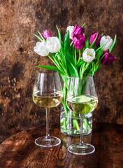 Cozy home still life - bouquet of colorful tulips and two glasses of white wine on a wooden table