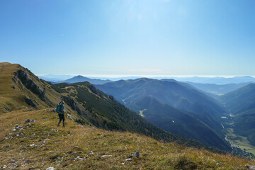 A woman with a hiking backpack hiking to the top of Hohe Weichsel in Austria. The woman in enjoying the calmness. The vast pasture is turning golden. Exploration and discovery. Endless mountain chains