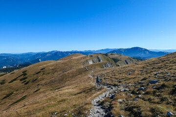 A woman with a hiking backpack hiking to the top of Hohe Weichsel in Austria. The woman in enjoying the calmness. The vast pasture is turning golden. Exploration and discovery. Endless mountain chains