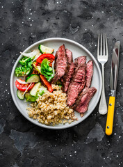 Delicious lunch - bulgur, lettuce, cucumber, tomato salad and steak on a dark background, top view