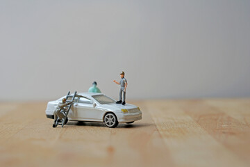 Miniature figurine character: Two mechanical engineers trying to fix white car; one using ladders and the car owner standing beside it
