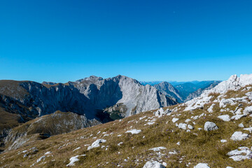 A panoramic view on Hochschwab mountain chains from the pathway leading to Hohe Weichsel. There is a vast pasture on top of a mountain, slowly turning golden. Clear view. Blue sky above. Autumn vibe