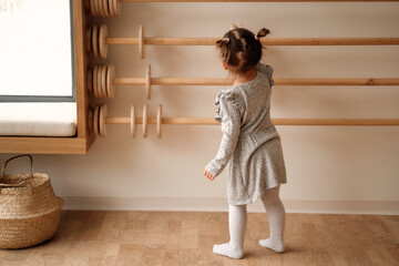 Little girl in a gray dress plays with wooden abacus in the children's room. Learns to count wooden...