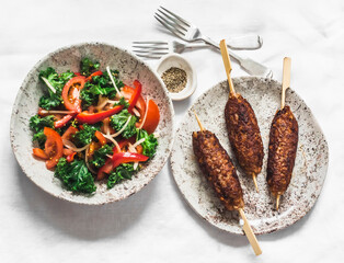 Fresh kale, tomatoes, bell pepper salad and beef kebab on a light background, top view. Delicious lunch