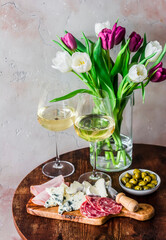 Delicious appetizers, tapas, snacks - ham, gorgonzola, camembert, salami, olives, white wine and bouquet of tulips on a wooden table