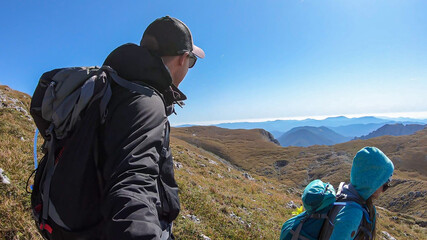 A couple with a hiking backpacks hiking to the top of Hohe Weichsel in Austria. They are enjoying the calmness and peace. Lush pasture around. Exploration and discovery. Endless mountain chains