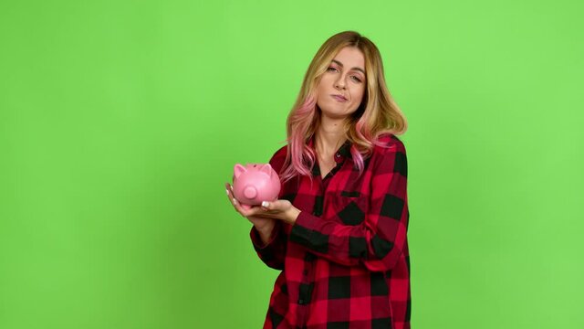 Young blonde woman happy and holding a piggybank over isolated background on green screen chroma key