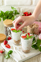 Female hands cooking healthy eating concept breakfast. Homemade granola with strawberry, yogurt, chia seeds, homemade granola and fresh berries on a wooden table.