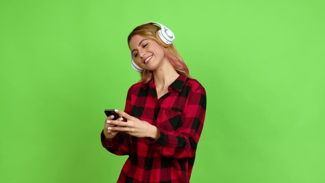 Young blonde woman listening to music with headphones over isolated background on green screen chroma key