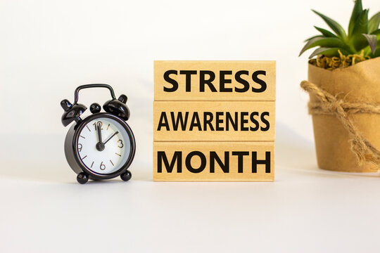 Stress awareness month symbol. Wooden blocks with words 'Stress awareness month'. Beautiful white background. Black alarm clock. Psychological, business and stress awareness month concept. Copy space.