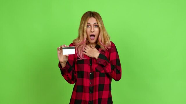 Young blonde woman surprised and holding a credit card over isolated background on green screen chroma key
